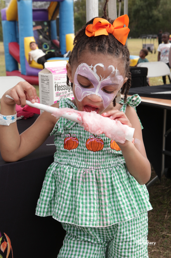 A girl with butterfly face paint biting into cotton candy