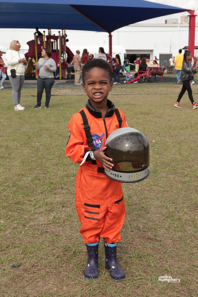 A boy in an orange astronaut costume holding his helmet